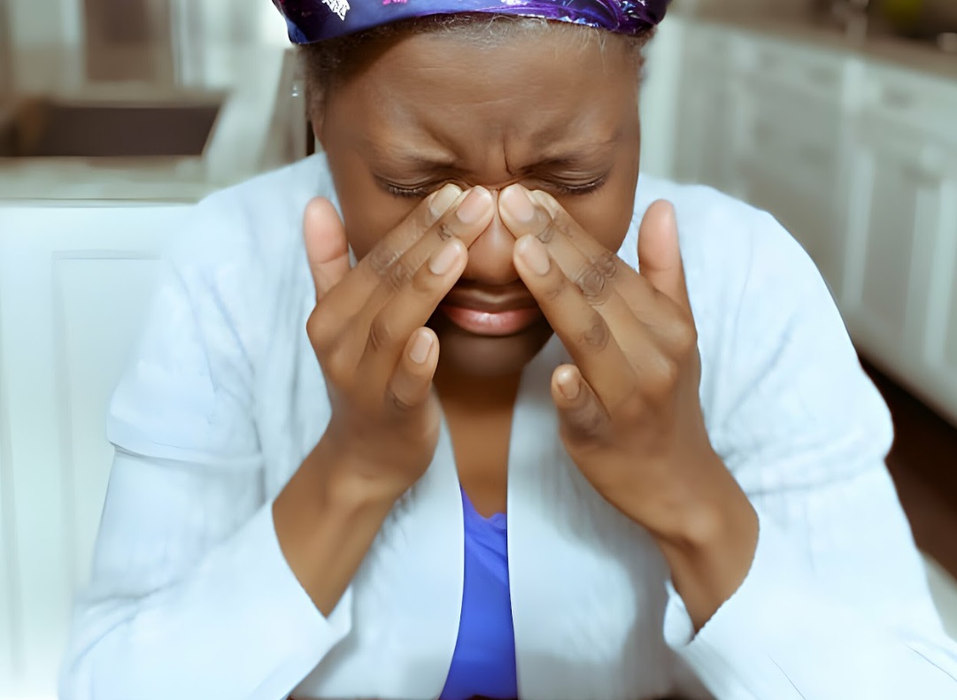 A black woman with her fingers on the bridge of nose presumably in pain from chronic rhinosinusitis